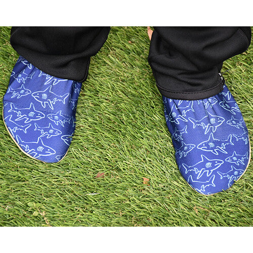 Voeten in blauwe waterschoentjes met haaienpatroon staan op groen gras.