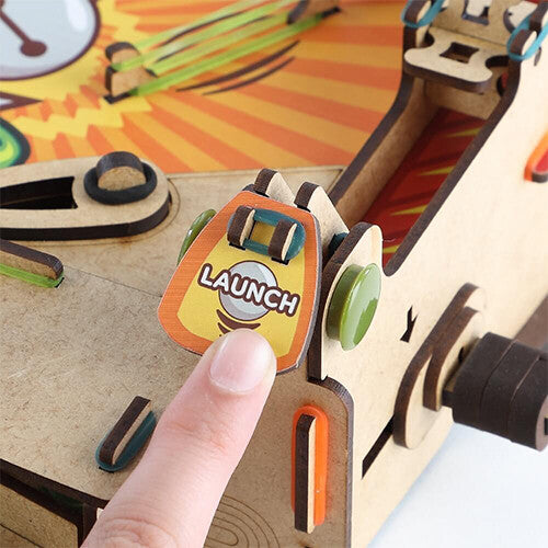 Detail van de Smartivity houten flipperkast bouwset, met een vinger die de 'LAUNCH' knop indrukt.