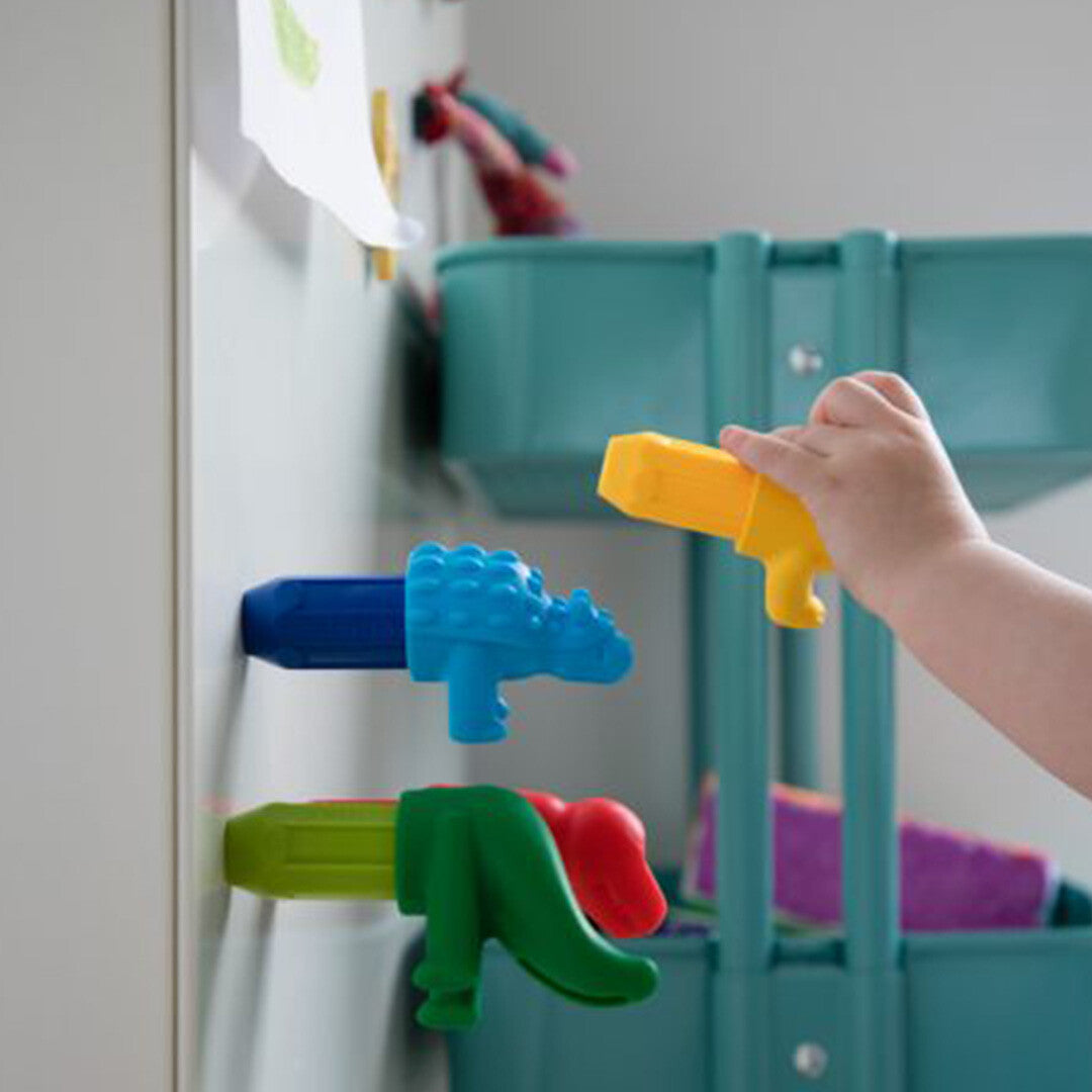 Een kinderhand bevestigt een geel dinosaurusonderdeel aan een blauw dinosauruslichaam op een witte muur.