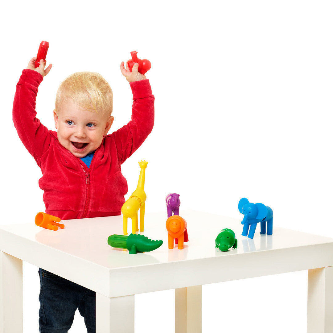 Een lachende peuter speelt met de SmartMax magnetische safaridieren aan een witte tafel.