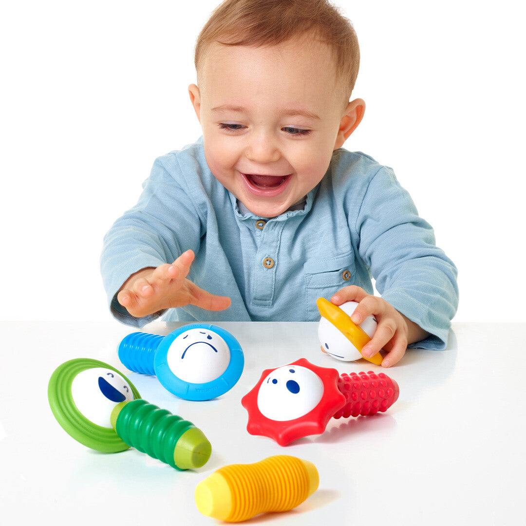 Een lachende baby speelt met de Smartmax My First Sounds & Senses rammelaars op een witte tafel.