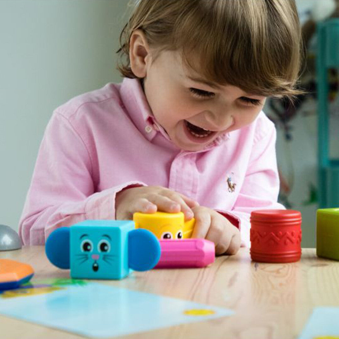 Een lachend kind speelt met de SmartMax magnetische stapelblokken aan tafel.