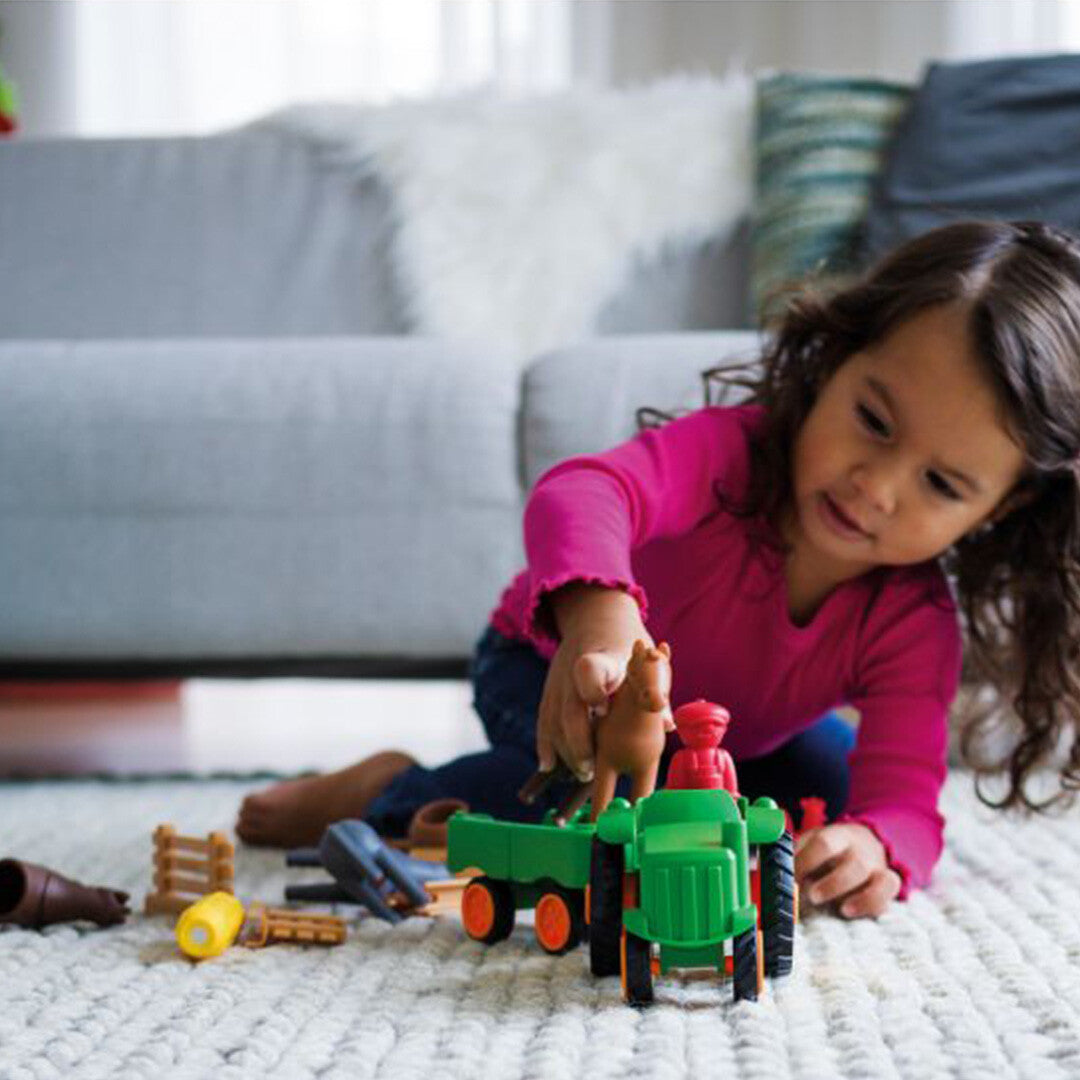 Een jong meisje speelt op de grond met de Smartmax My First Tractor Set.