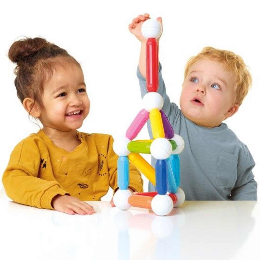 Twee jonge kinderen kijken naar een kleurrijk SmartMax magnetisch bouwsel op tafel.