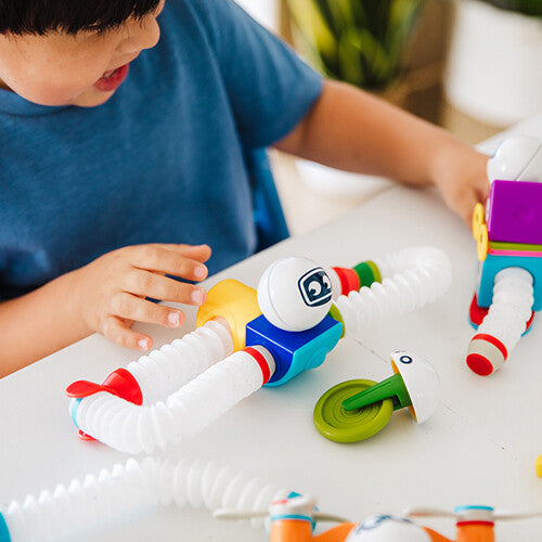 Een kind speelt met de Smartmax Roboflex bouwset op een witte tafel, bezig met het bouwen van een flexibele robot.