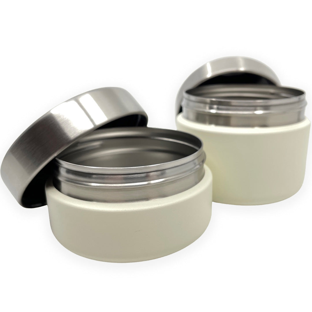 Twee open Smikkels voedselpotten in crème met zilverkleurige deksels, die de roestvrijstalen binnenkant tonen.