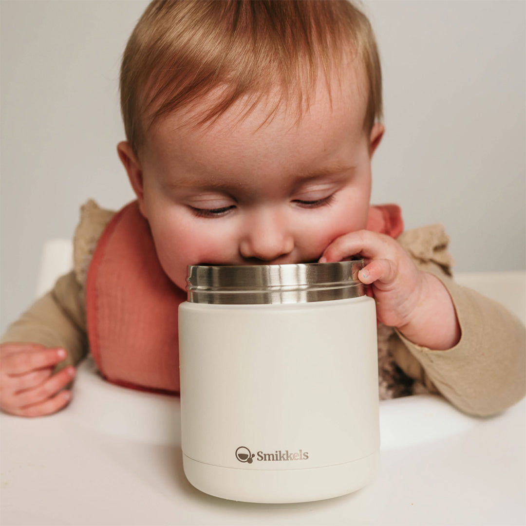 Een baby kijkt in de Smikkels crème thermos voedselpot.