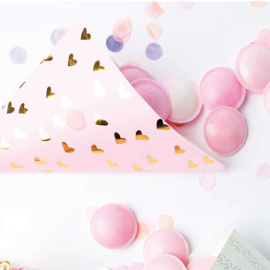 Roze papieren puntzakje met gouden hartjes, gevuld met roze snoepjes en confetti.