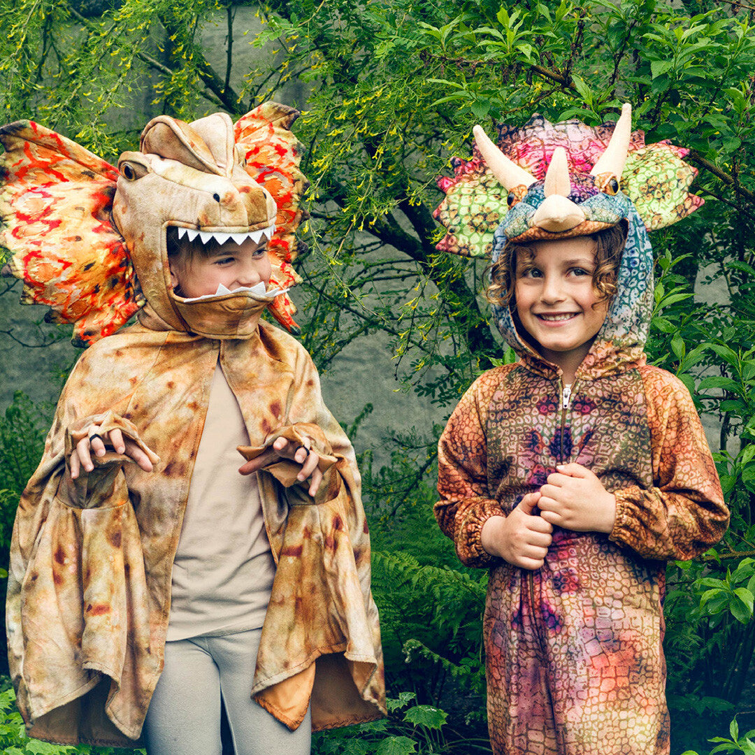 Twee kinderen in dinosaurus kostuums, waaronder de Souza for kids dilophosaurus cape, in een groene tuin.