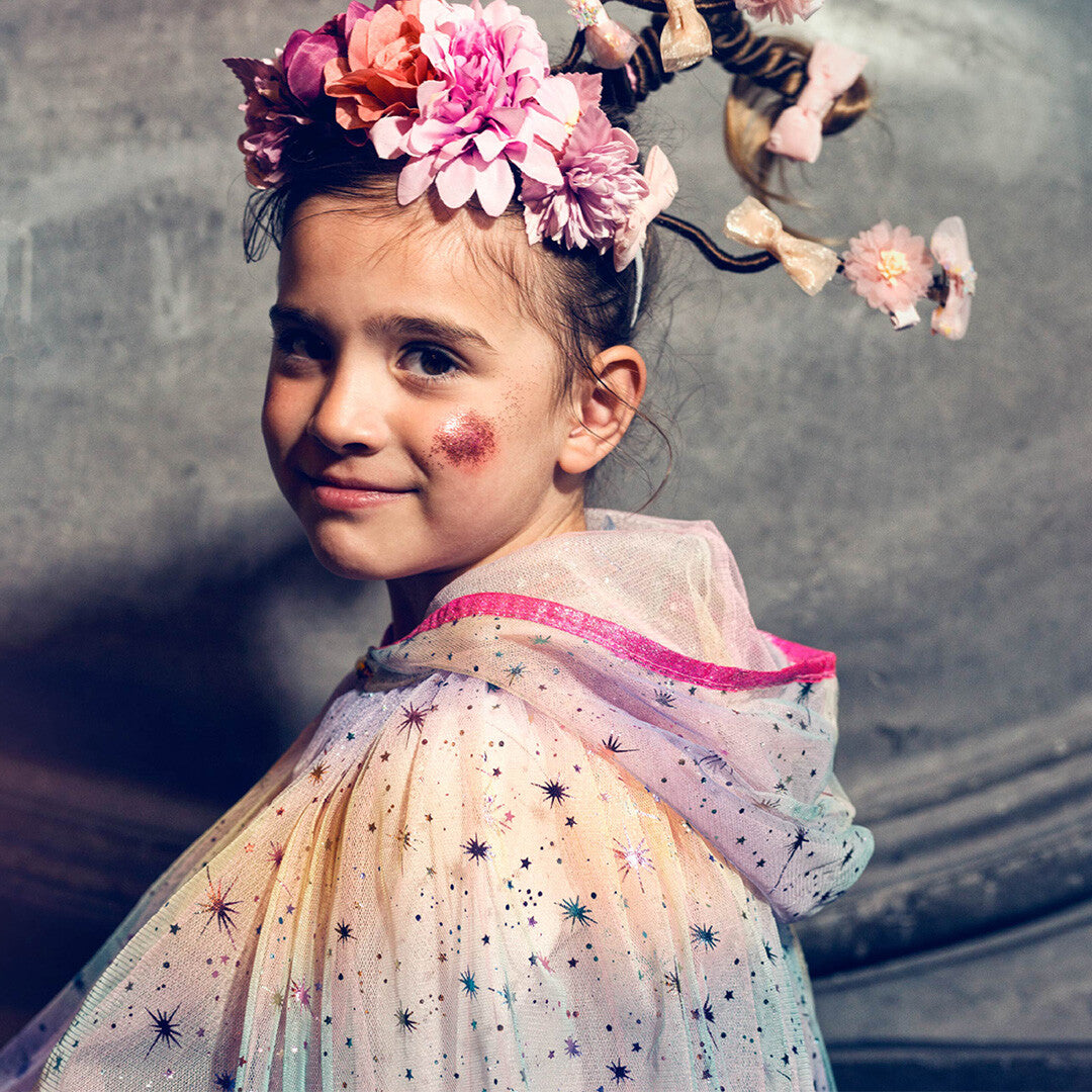 Close-up van een kind met de regenboog cape met sterren en bloemen in het haar.