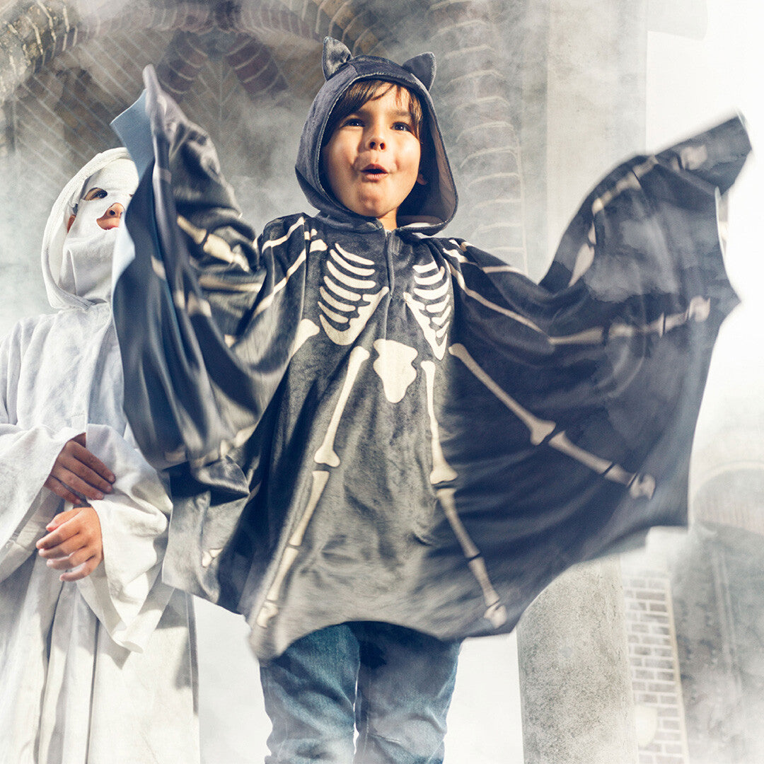 Een kind draagt de Souza for Kids vleermuis cape met skeletprint en spreidt de armen.
