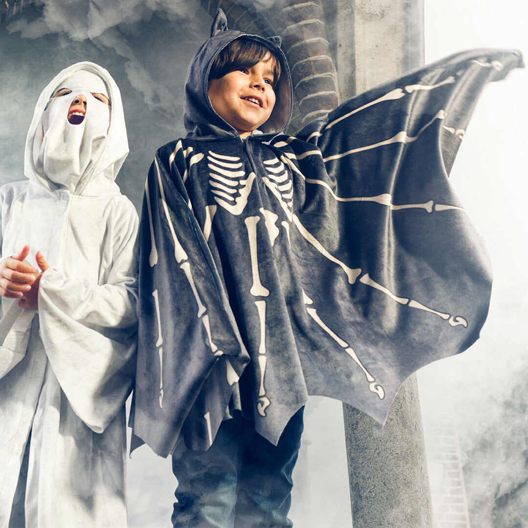 Twee kinderen poseren in kostuums, waarvan één de Souza for Kids vleermuis cape met skeletprint draagt.