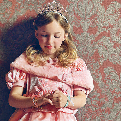 Meisje met de roze diadeem en een prinsessenjurk kijkt naar haar handen.