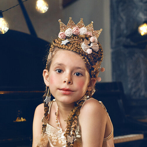 Een meisje draagt de gouden glitterkroon diadeem met roze en witte bloemen in haar gevlochten haar.