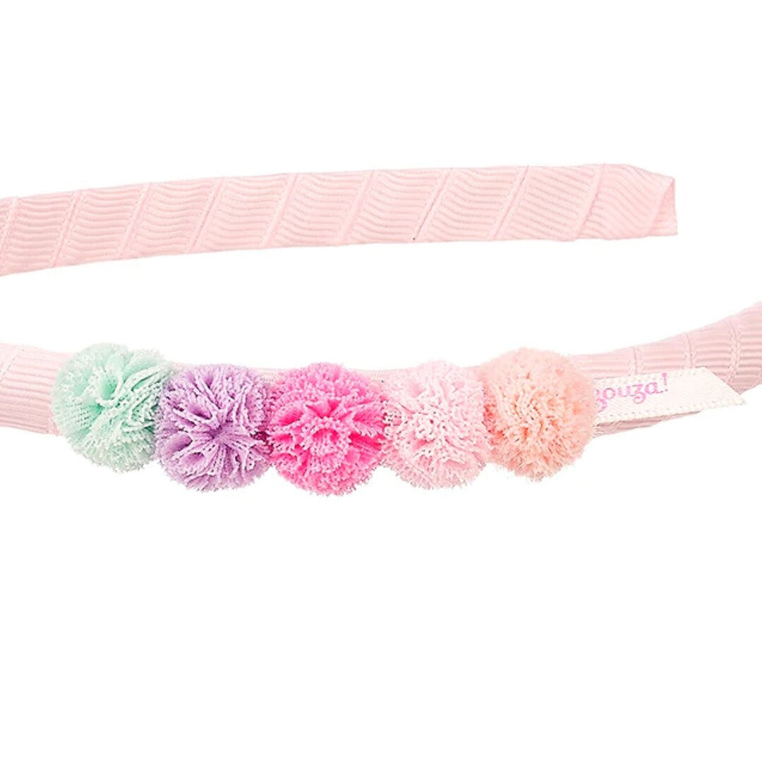 Detail van de roze kinder hoofdband met vijf gekleurde pompons en een wit label.