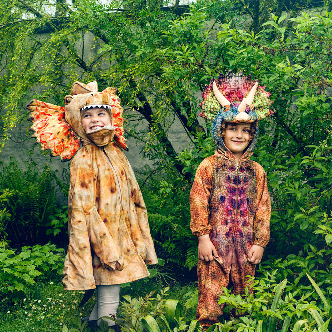 Twee kinderen in dinosaurus kostuums, waaronder het Souza for kids triceratops dinopak, staan lachend in een groene tuin.