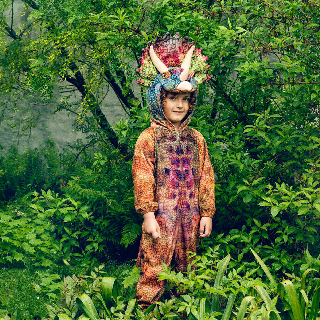 Een kind draagt het Souza for Kids triceratops kinderkostuum en staat lachend in een groene tuin.