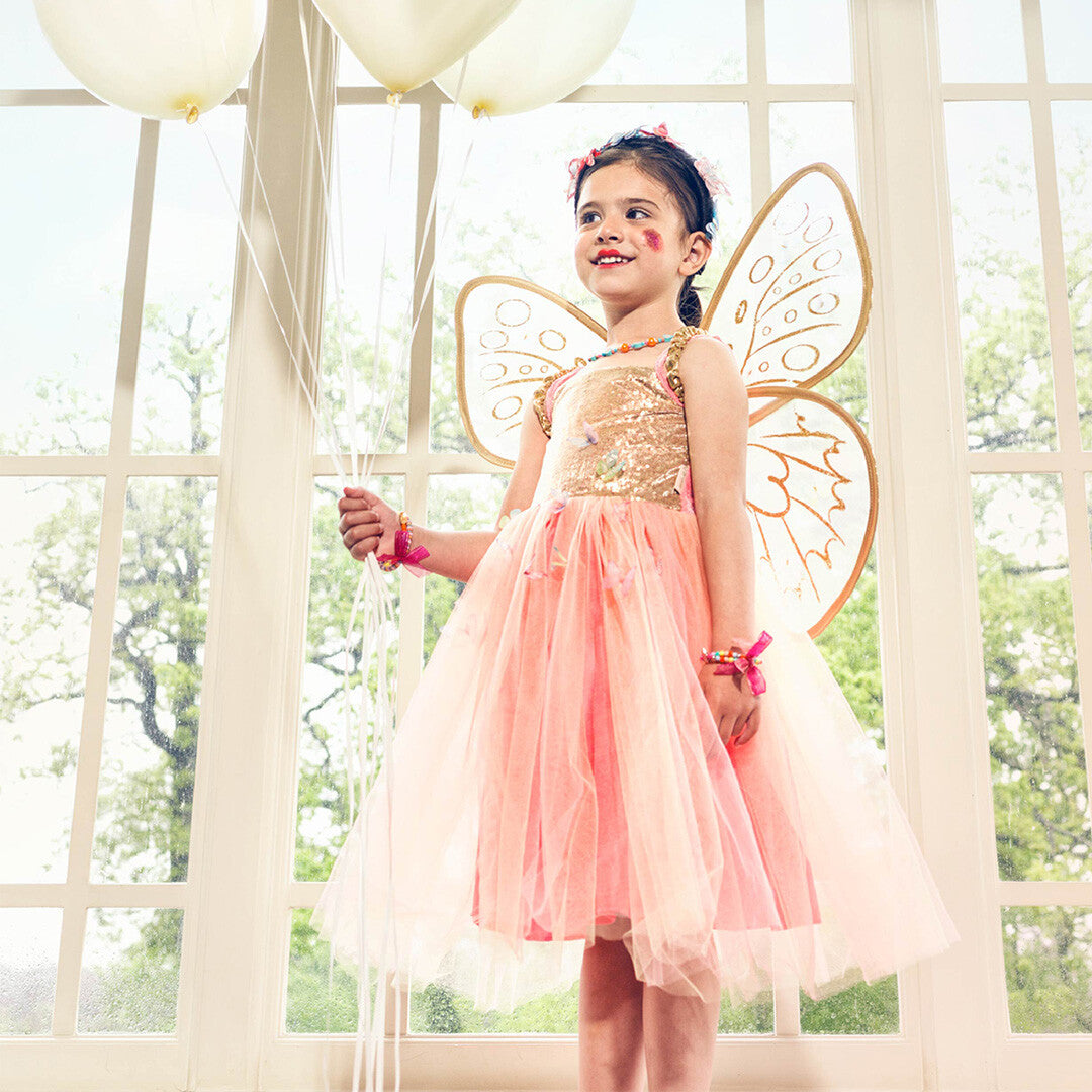 Een meisje draagt de Souza for Kids elfenjurk Joanna met vleugels en houdt witte ballonnen vast.