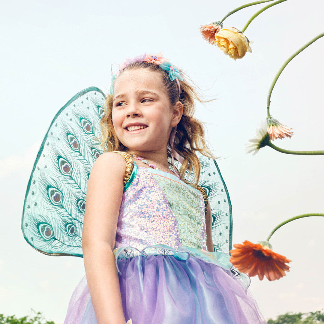 Een lachend meisje draagt de souza for kids elfenjurk Tamara met pauwenveren vleugels en een bloemenhaarband.
