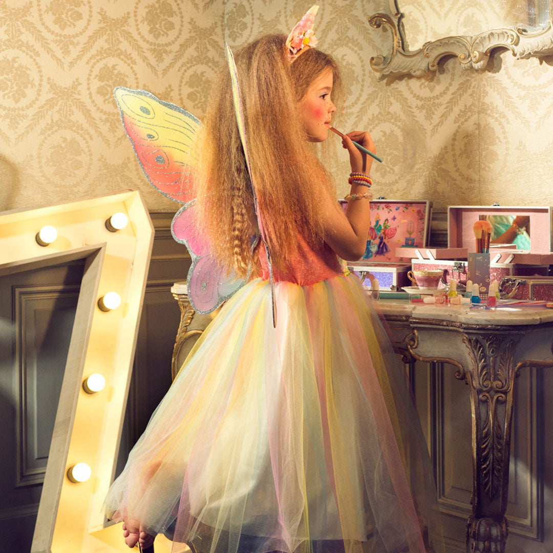 Een meisje in de Souza for Kids elfenjurk Valerie met vlindervleugels doet make-up op voor een spiegel.