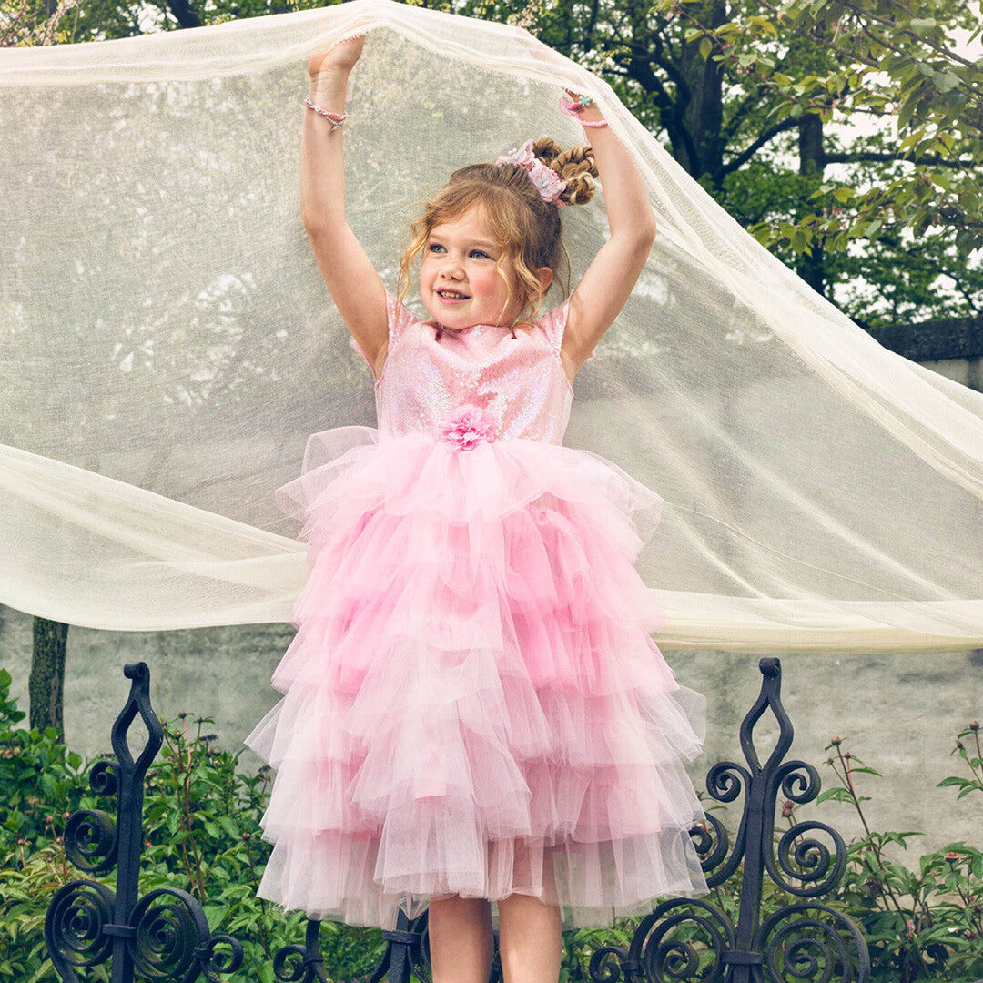 Een meisje draagt de roze prinsessen feestjurk en houdt een doorschijnende doek boven haar hoofd in een tuin.