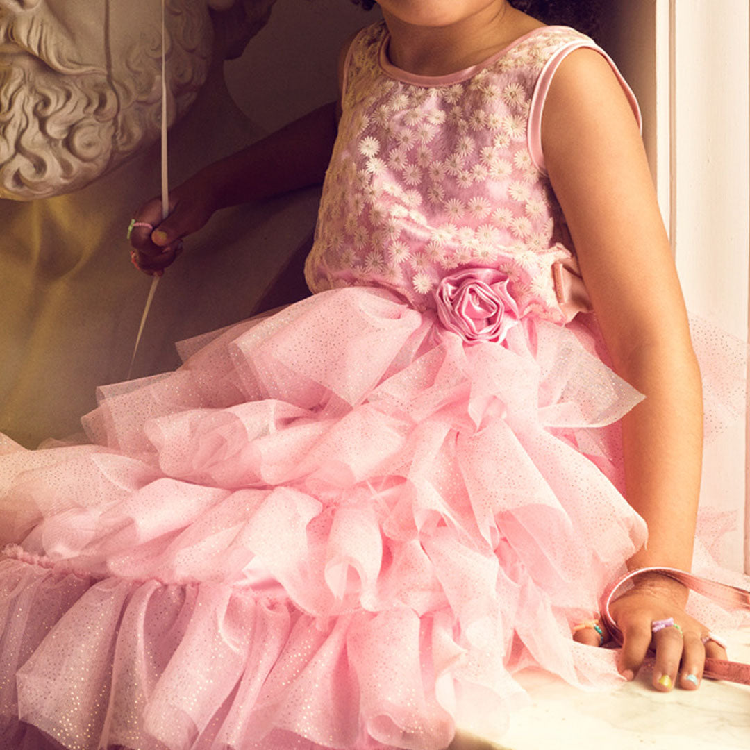 Detailfoto van de roze prinsessenjurk met gelaagde tule rok en een roos op de taille, gedragen door een meisje.