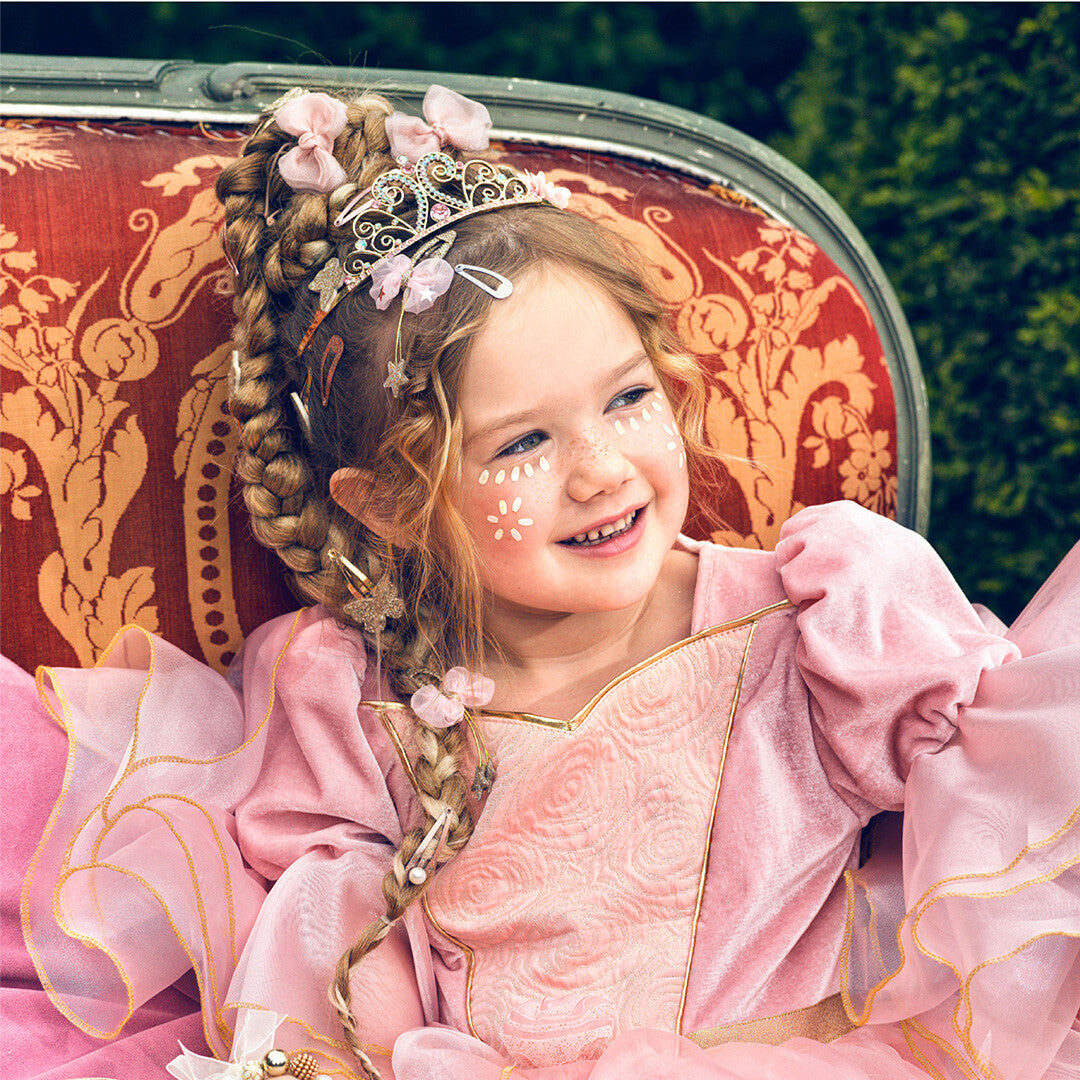 Een lachend meisje draagt de Souza for Kids roze prinsessen kostuumjurk met tiara en gezichtsverf.
