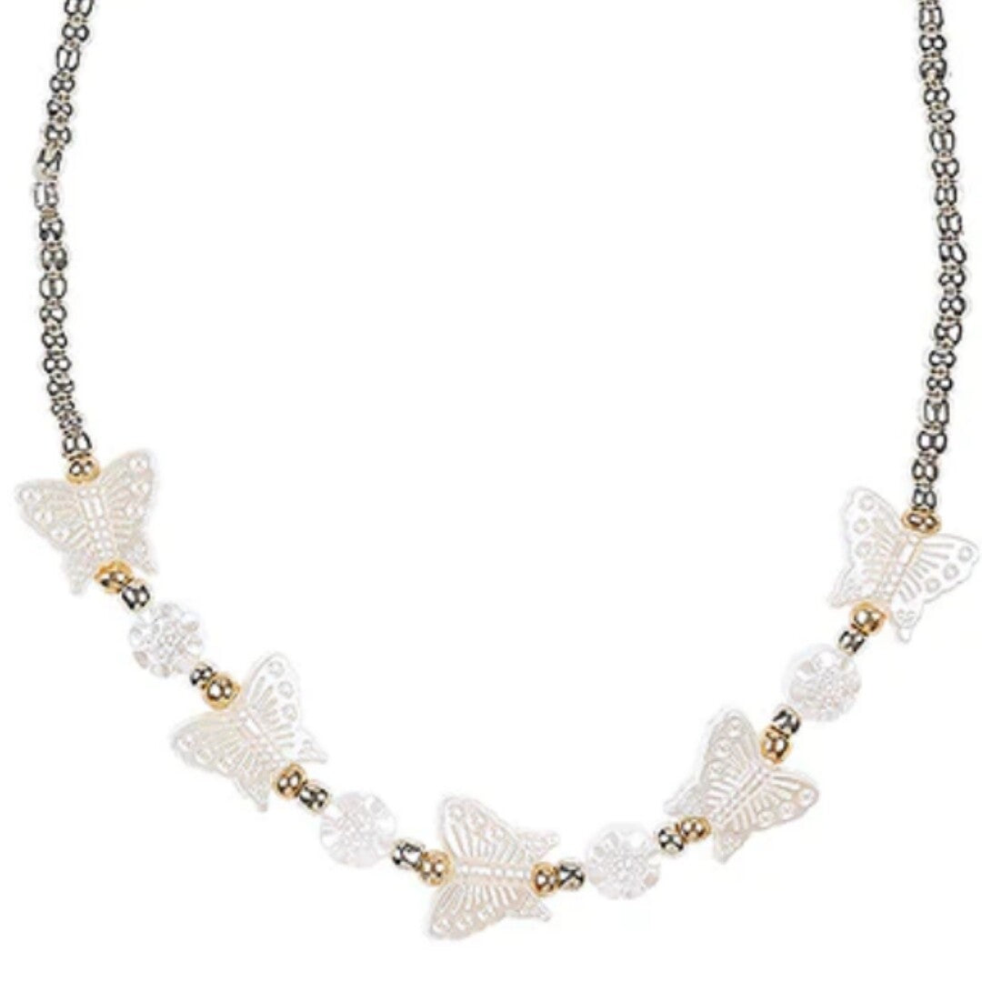 Detailopname van de kinderketting met witte vlinderkralen en gouden accenten.