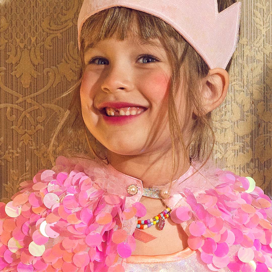Close-up van een lachend meisje met de roze verkleedcape met schubben en een ketting.