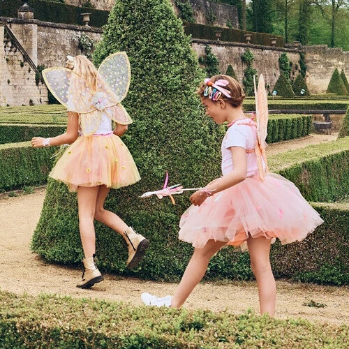 Twee meisjes met roze Souza for Kids vleugels en tutu's spelen in een tuin.