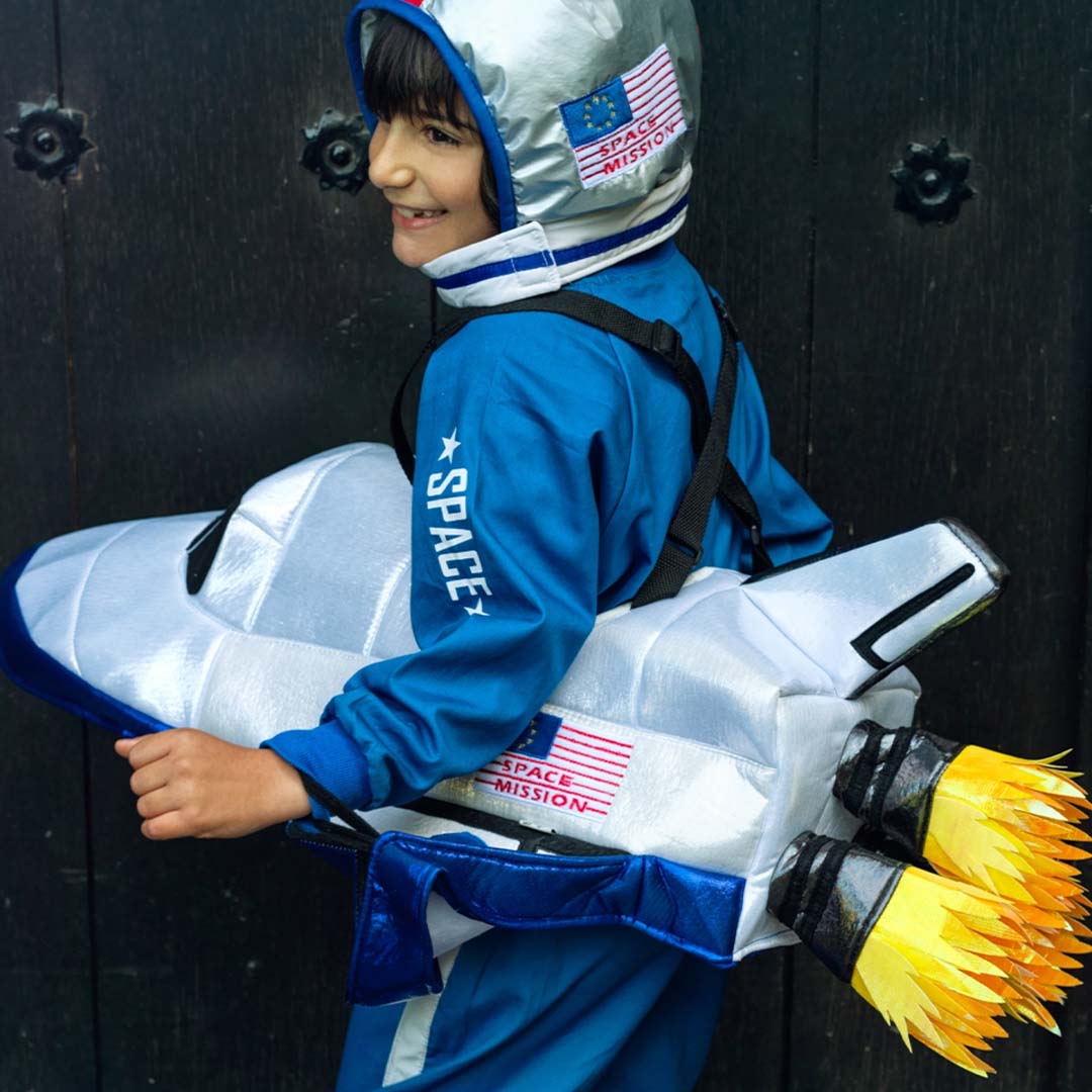 Zijaanzicht van een kind met de Souza for Kids zilveren ruimtehelm en blauw ruimtepak, met de achterkant van de spaceshuttle inclusief vlammen.