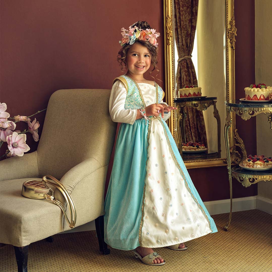 Een lachend meisje draagt de blauw-witte prinsessen verkleedjurk met een bloemenkrans op haar hoofd.