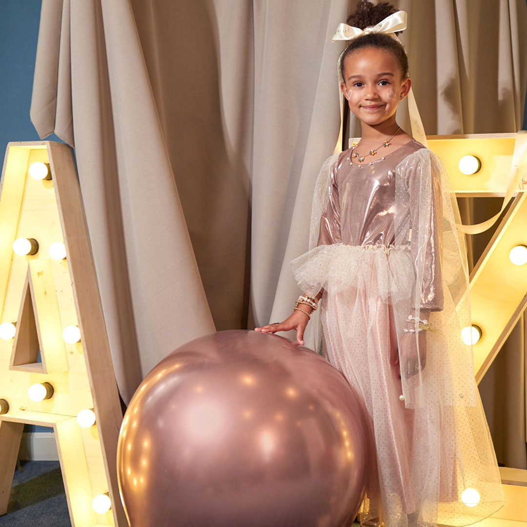 Meisje in de Souza for Kids prinsessen verkleedjurk Philou staat naast een grote roségouden ballon.