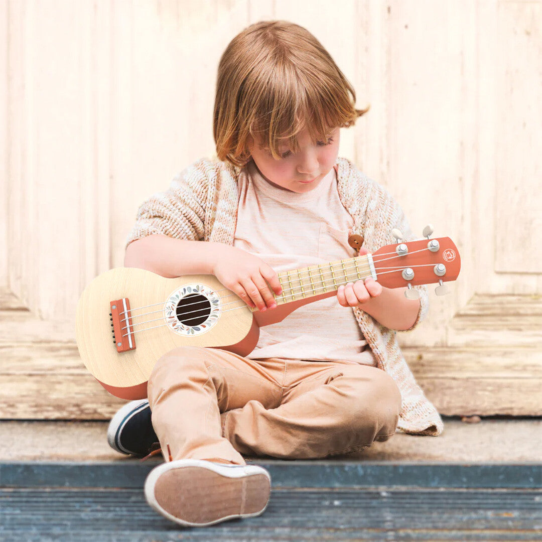 Een kind zit op treden en speelt op de Speedy Monkey houten speelgoed ukelele.