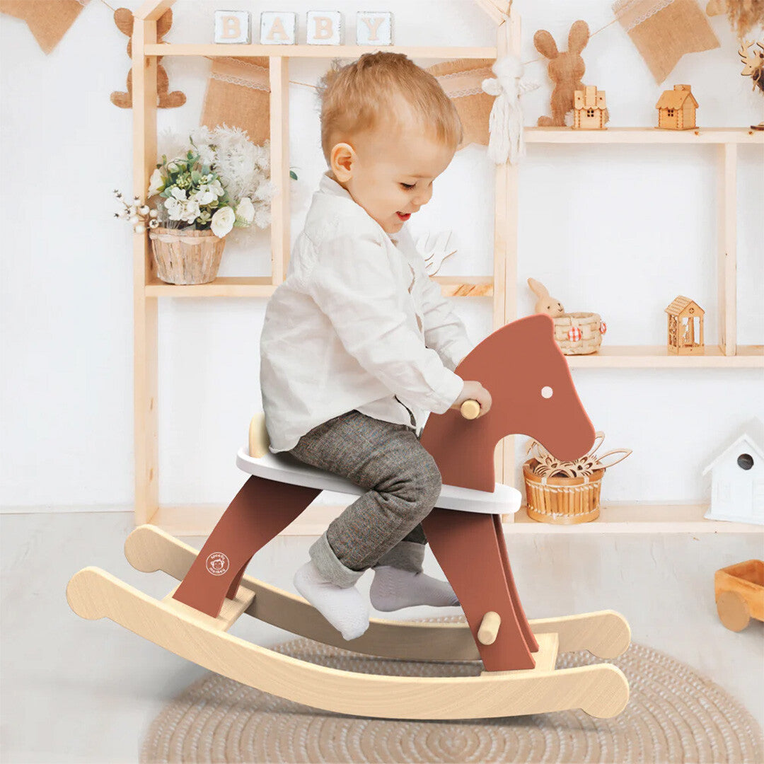 Een lachende peuter zit op het Speedy Monkey houten hobbelpaard in een kinderkamer.