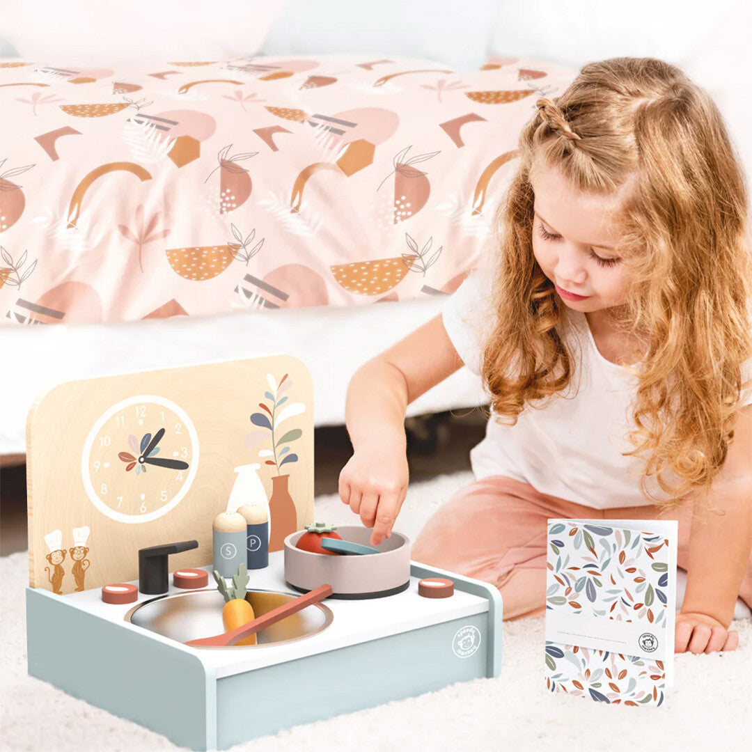 Een meisje speelt met de Speedy Monkey houten kinderkeuken tafelmodel, roerend in een pan met speelgoedeten.