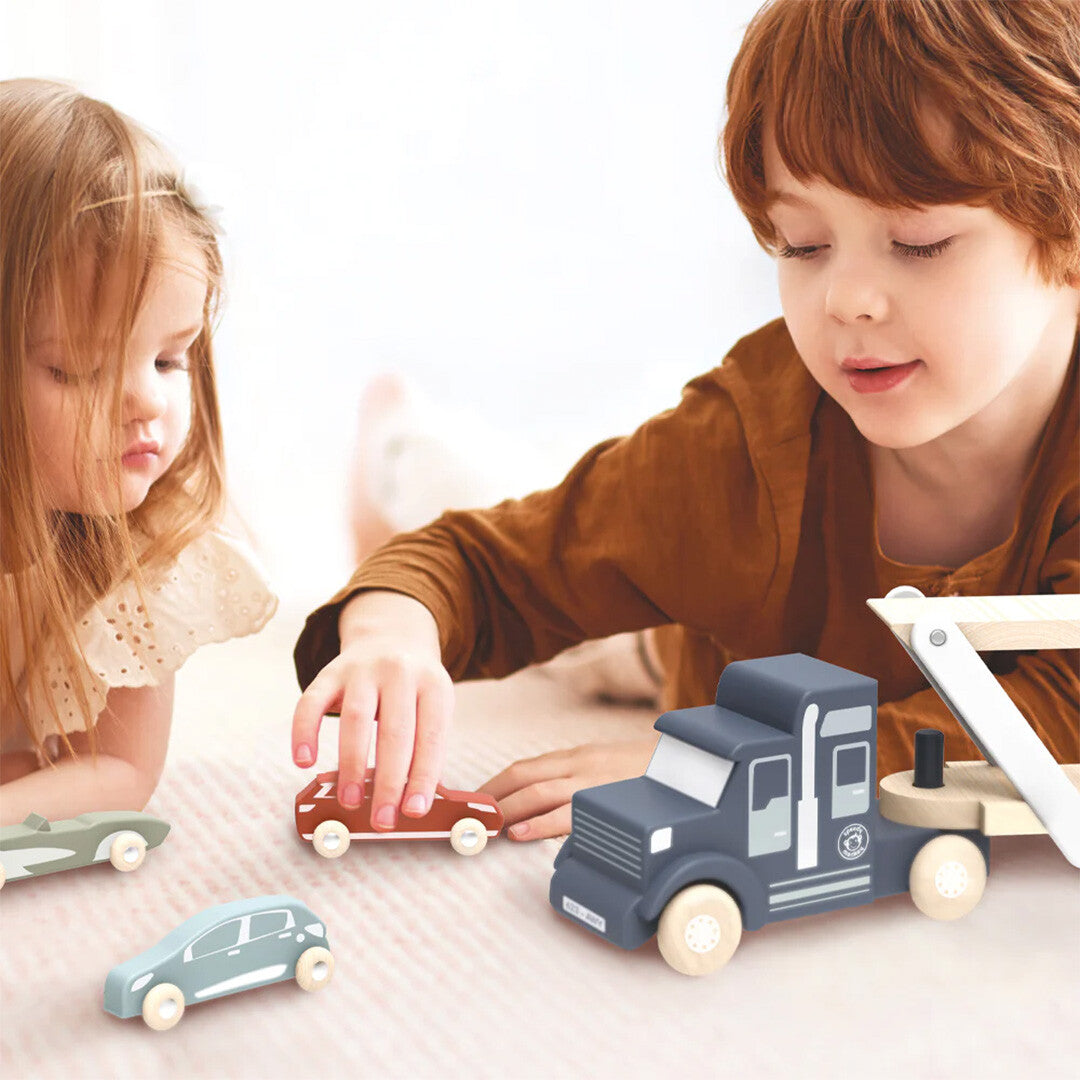 Twee kinderen spelen op de grond met de houten speelgoedtransportwagen en auto's.