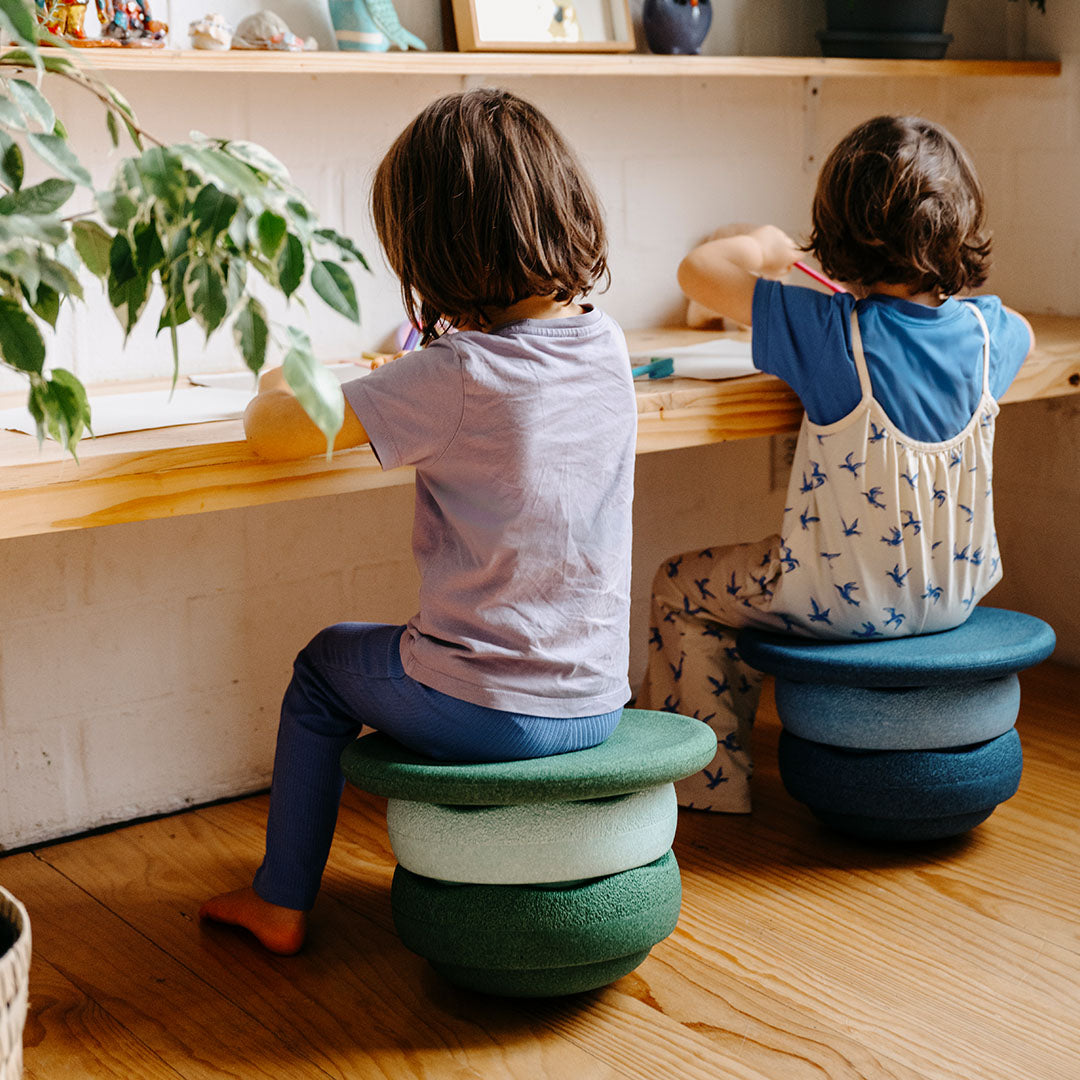 Twee kinderen zitten aan een tafel, elk op een stapel Stapelstein elementen als zitje.