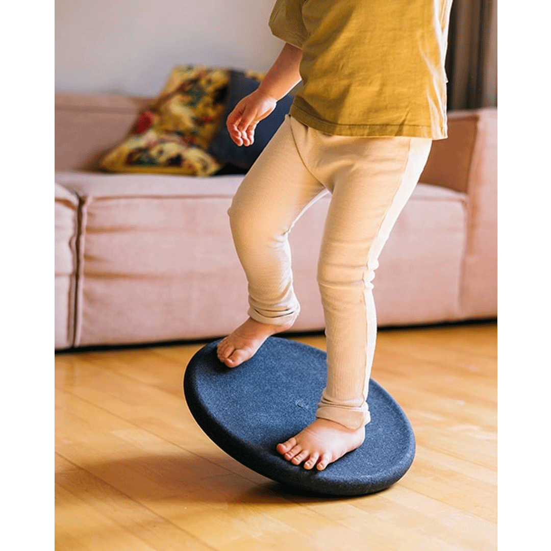 Een kind staat blootsvoets op een Stapelstein balance board in een woonkamer.