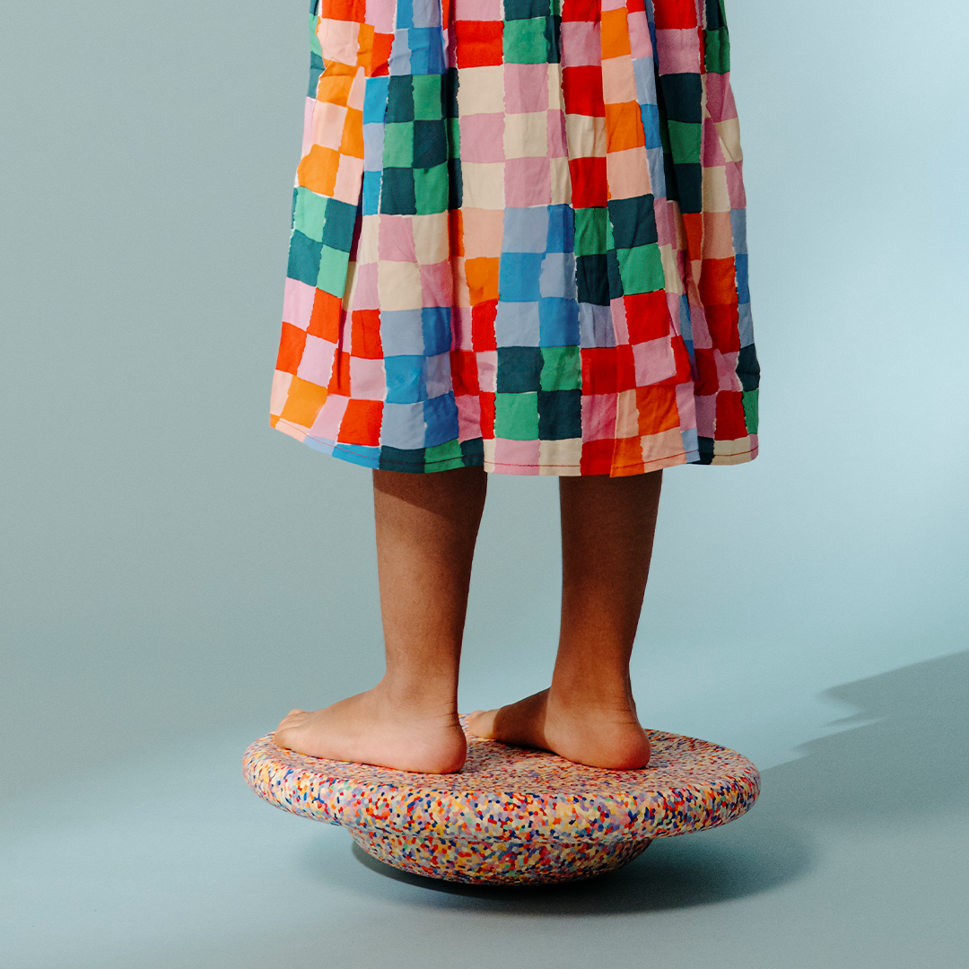 Een kind staat met blote voeten op het stapelstein balance board met confetti patroon.