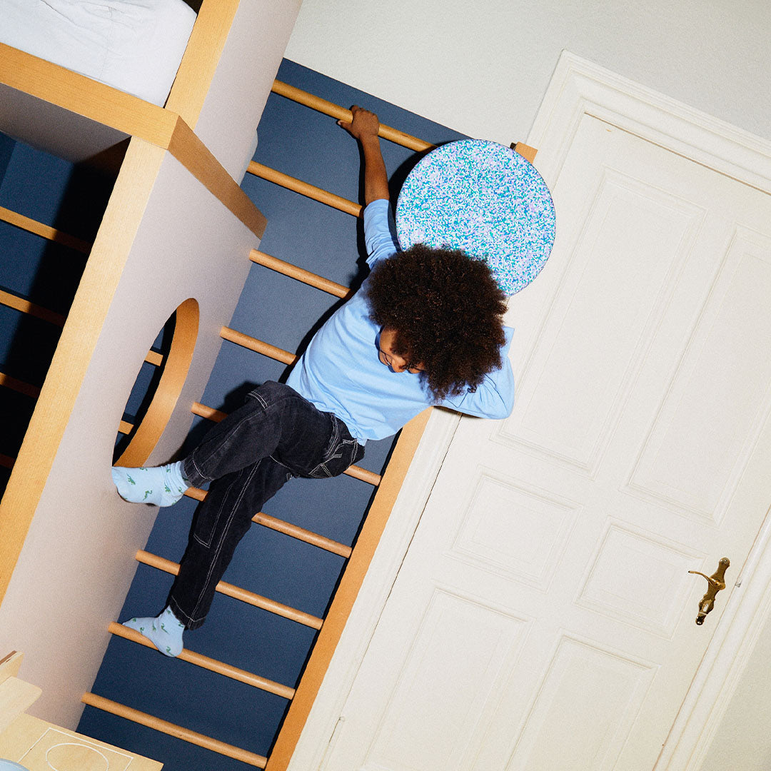 Een kind klimt op een houten klimrek en houdt een stapelstein balance board met mozaïekpatroon vast.