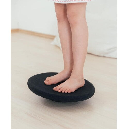 Kind staat met blote voeten op een zwart stapelstein balance board.