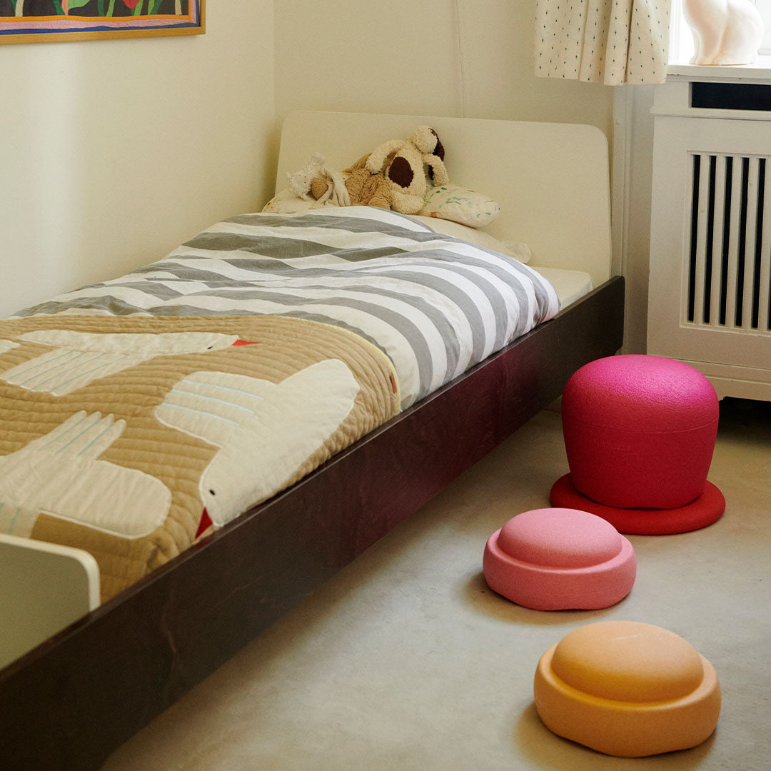 Drie Stapelstein dynamic flowers schuimrubberblokken liggen verspreid op de vloer in een kinderkamer naast een bed.