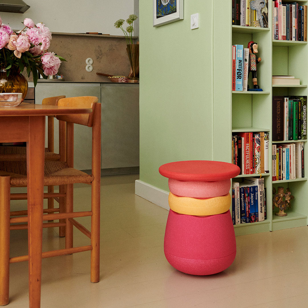 Een stapel Stapelstein dynamic flowers schuimrubberblokken staat op de vloer naast een houten tafel en een groene boekenkast.