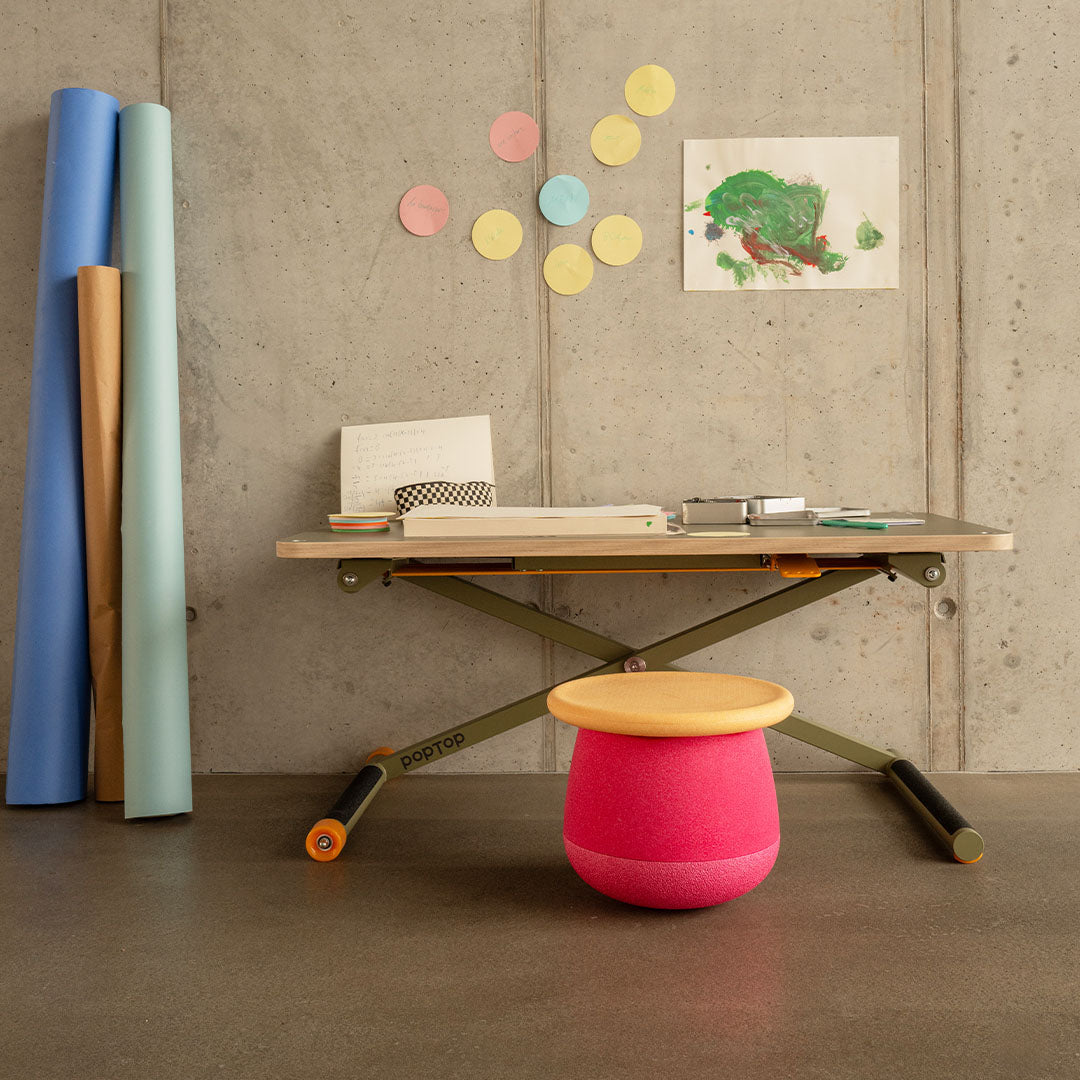 Een roze stapelstein dynamic small staat als krukje voor een bureau tegen een betonnen muur.