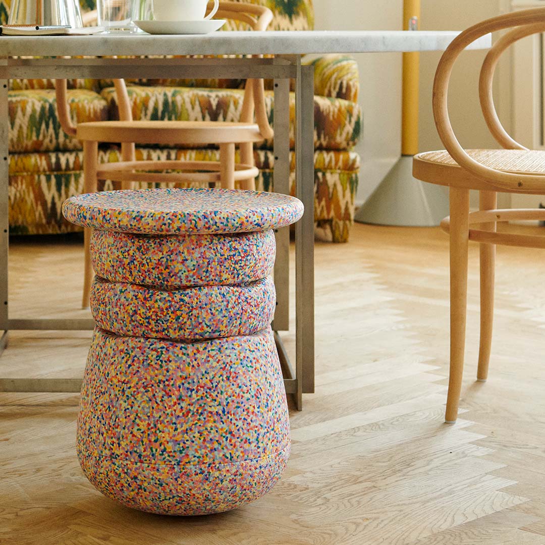Een stapelstein dynamic confetti element staat op een houten vloer in een woonkamer, naast een tafel en stoelen.