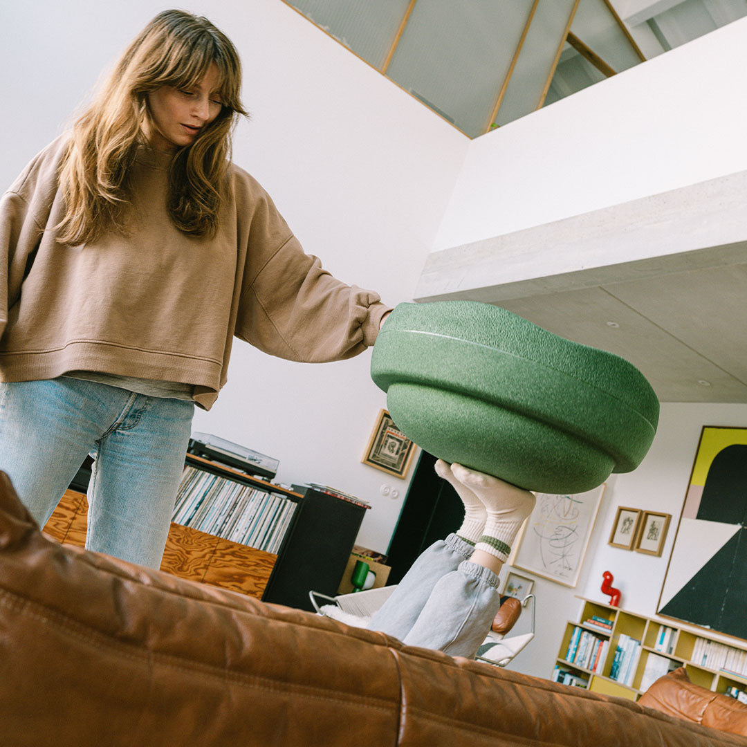 Een vrouw houdt een stapelstein original GROW donkergroene stapelsteen vast, met op de achtergrond een woonkamer.