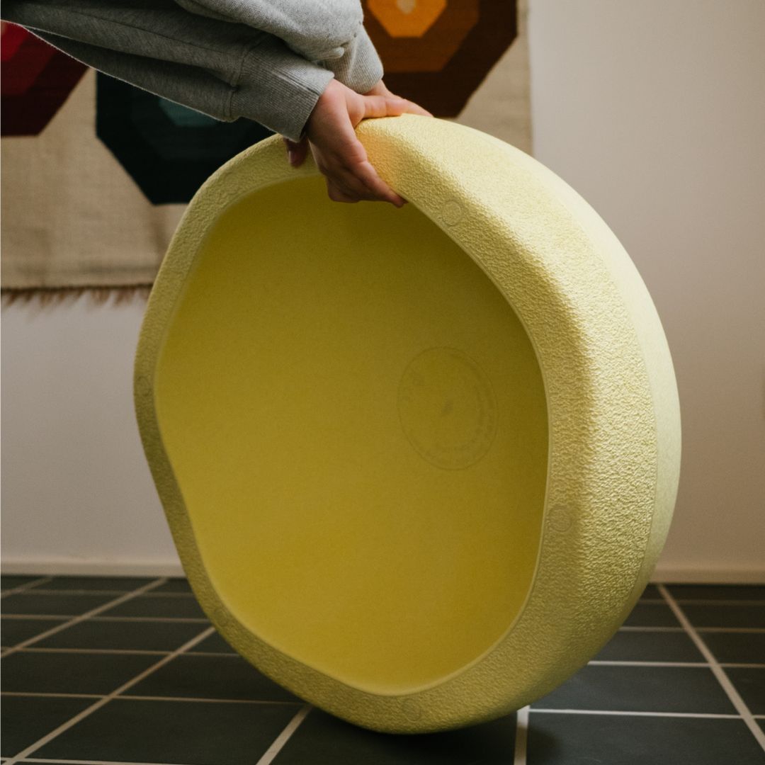 Een persoon houdt een lichtgele stapelstein schuimrubberblok vast, met de holle onderkant zichtbaar.