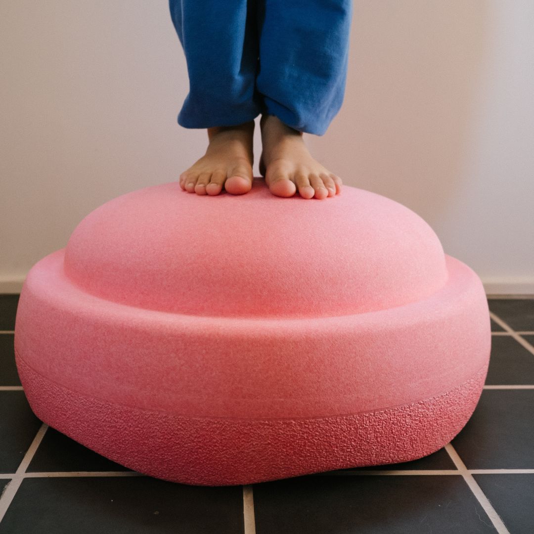 Blote kindervoeten staan op een lichtroze stapelstein schuimrubberblok.