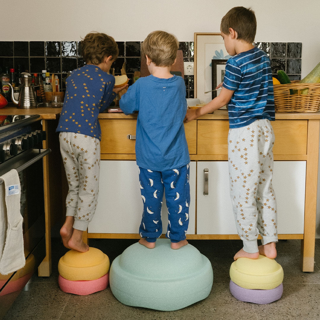 Drie kinderen staan op gekleurde stapelstein speelelementen om bij een aanrecht te komen.